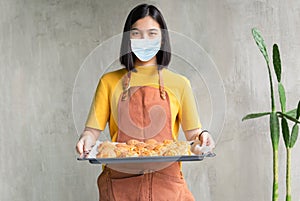 Woman in medical mask holding baking tray with choux cream SME concept.