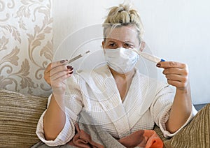A woman in a medical mask is holding an electronic and mercury thermometer.