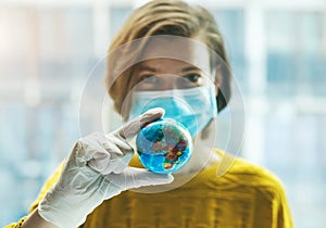 Woman in medical mask holding global earth model in hand in gloves