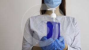 Woman with a medical mask and latex glove holding bottle of alcohol gel