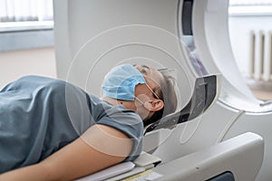 A woman in a medical mask lies on the tomograph table. woman is undergoing computed axial tomography examination in a