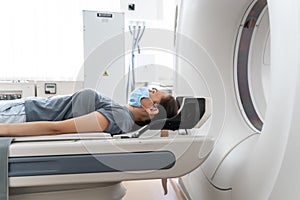 A woman in a medical mask lies on the tomograph table. woman is undergoing computed axial tomography examination in a
