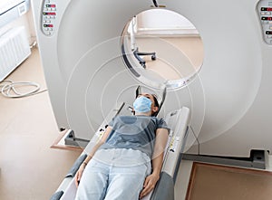 A woman in a medical mask lies on the tomograph table. woman is undergoing computed axial tomography examination in a