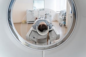 A woman in a medical mask lies on the tomograph table. woman is undergoing computed axial tomography examination in a