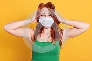 Woman in medical mask plugging ears with hands. European young redhead female ignoring noise or news about coronavirus, wearing