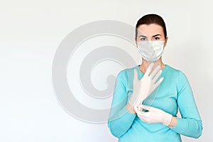 Woman in medical mask puts on rubber surgical gloves. Shot on a light background, medium plan, copy space.