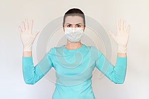 Woman in medical mask and rubber gloves in a blue sweater on a white background looking at the camera. The concept of safety