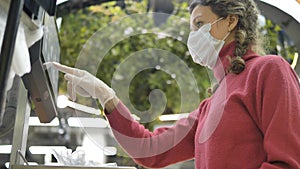 Woman in a medical mask and rubber gloves weighs goods on an electronic scale in a supermarket. Protection from the
