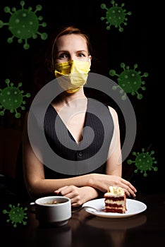 A woman in a medical mask sits at a table with tea and a cake. Molecules of coronavirus fly around. Virus protection in a public