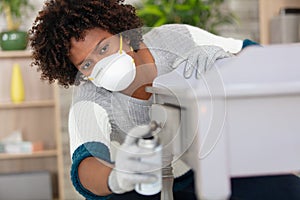 woman in medical mask sprays disinfectant on closet