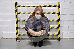 A woman in a medical mask is standing in a dead end near a yellow-and-black-striped security fence, concept