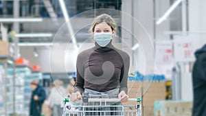 A woman in a medical mask stands in a supermarket with a grocery cart. Protection from coronavirus, buying food in a