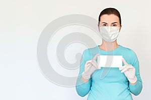 A woman in a medical mask and surgical gloves holds a small white tablet with place for text. Shot on a light background