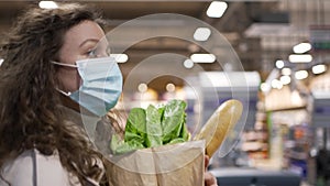 Woman in a medical mask walks through the supermarket with a paper bag with purchases in slow motion