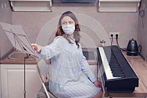 A woman in a medical mask watches music and plays a digital piano at home. Learning music in the period of the pandemic in