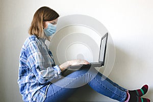 Woman in medical mask is working from home. Online freelance during the time of quarantine. Laptop in hands. Coronavirus pandemia