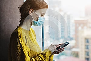 Woman in medical mask working with phone at home quarantine