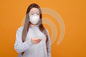 woman in medical mask on a yellow background, coronavirus pandemic, woman looks at thermometer, emotions