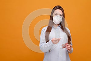 woman in medical mask on a yellow background, coronavirus pandemic, woman looks at thermometer, emotions, pills in hand