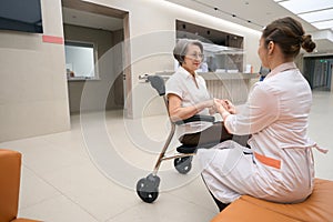 Woman in a medical outfit greets a patient in wheelchair