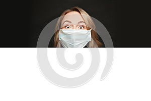 Woman in medical protective face mask with white empty paper signboard banner on black background