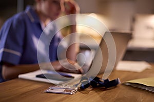 Woman In Medical Uniform Working Or Studying On Laptop At Home At Night With Security ID Lanyard