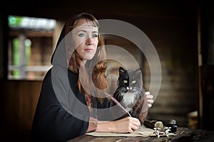 A woman in a medieval cloak sits with a pen and writes.