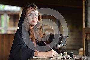 A woman in a medieval cloak sits with a pen and writes.