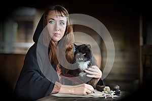 A woman in a medieval cloak sits with a pen and writes.