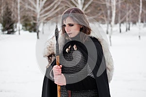 The woman is a medieval warrior of the Viking Age in the winter in the forest.