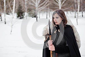 The woman is a medieval warrior of the Viking Age in the winter in the forest.