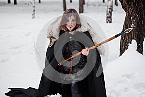 The woman is a medieval warrior of the Viking Age in the winter in the forest.