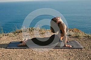 Woman meditates while practicing yoga exercises in the mountains against the background of the sea.