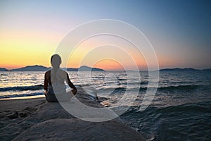 Woman meditates - relaxes at sunset by the sea on the beach. Concept for yoga, health and spa