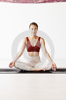 A woman meditates in a yoga studio. She is in Siddhasana