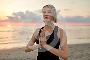 woman meditating on beach over sunset