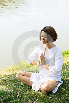 Woman meditating in easy pose on the grass at the river-bank. photo