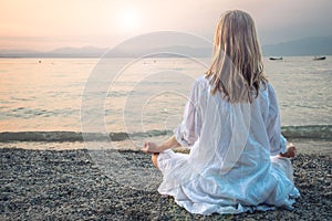 Woman meditating at the Garda Lake. Sunset.