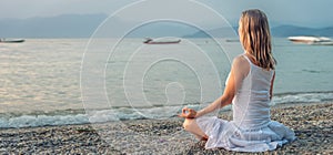 Woman meditating at the Garda Lake. Sunset.