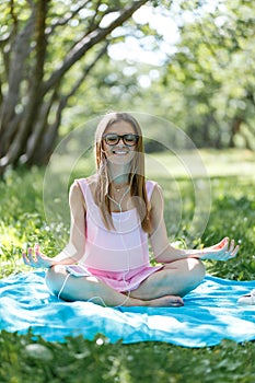 Woman meditating on green grass at the park sitting in lotus position. Fitness girl relaxing in yoga pose after exercises