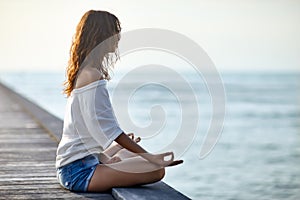 Woman meditating in Lotus Pose on pier