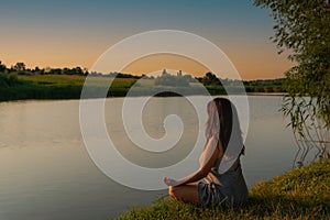 Woman meditating in lotus pose during sunset. Girl meditates on shore of river alone with herself. Yoga, meditation