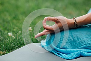 Woman meditating in lotus position closeup. Hands close-up mudra. Sitting on rug the lawn of green grass background