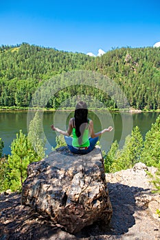 Woman meditating in lotus posture doing yoga on top of the mountain on a rock.