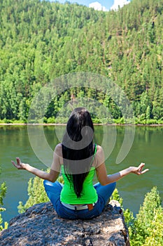 Woman meditating in lotus posture doing yoga on top of the mountain on a rock.