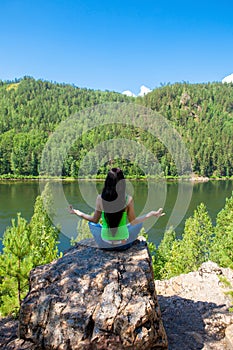 Woman meditating in lotus posture doing yoga on top of the mountain on a rock.