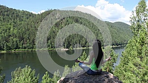 Woman meditating in lotus posture doing yoga on top of the mountain on a rock.