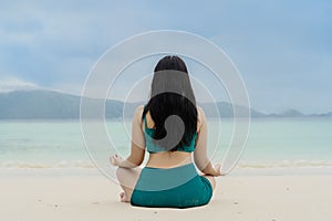 Woman meditating in lotus yoga on coast of sea on the beach. Peaceful healthy and fit young woman meditating on the beach. Woman