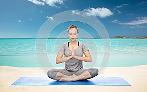 Woman meditating in lotus yoga pose on beach