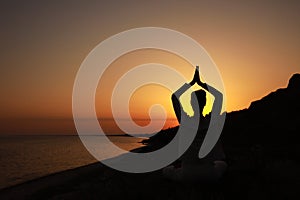 Woman meditating near sea at sunset, back view. Space for text